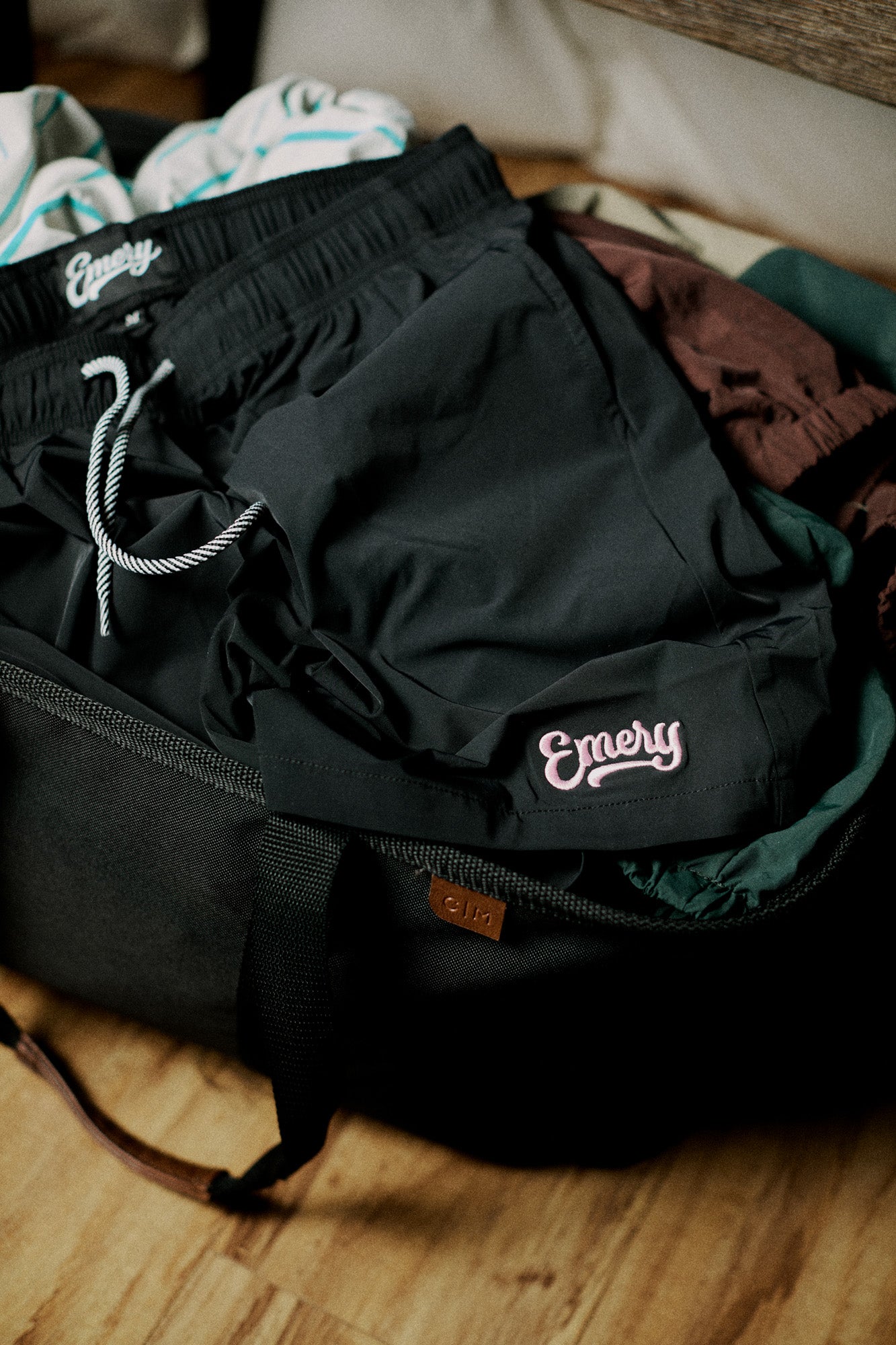 Black shorts with 'Emery' branding on a wooden surface