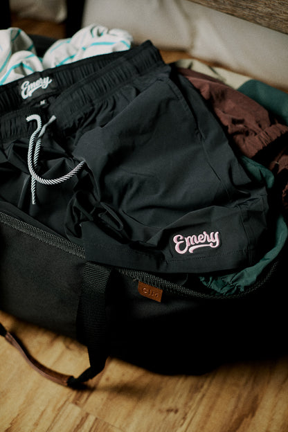 Black shorts with 'Emery' branding on a wooden surface